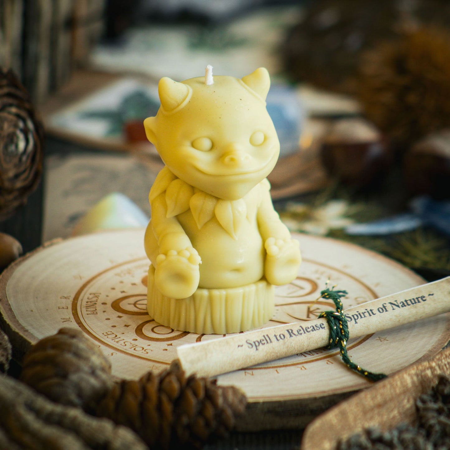 A light green candle in the shape of a magical nature sprite sits behind a rolled up spell to celebrate Beltane and mayday