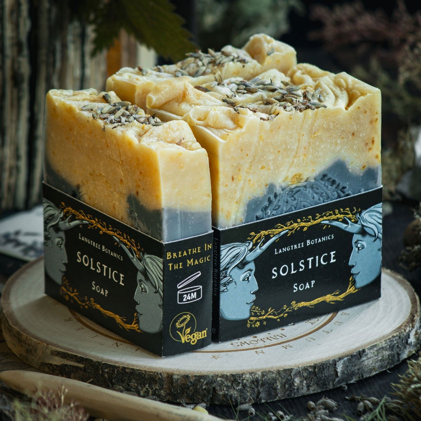Langtree Botanics summer collection of four Solstice Soap Bars on a decorative log slice surrounded by seasonal foliage