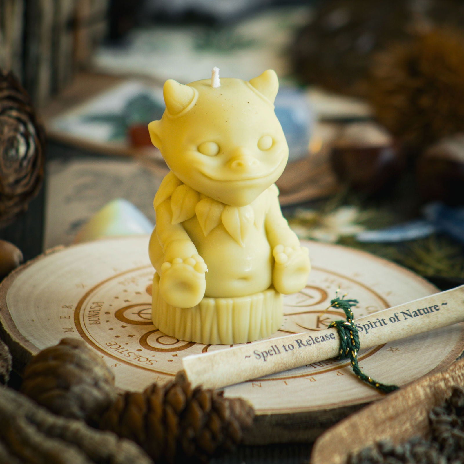 A light green candle in the shape of a magical nature sprite sits behind a rolled up spell to celebrate Beltane and mayday  