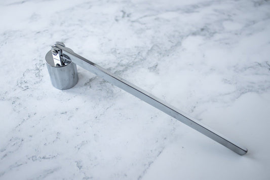 A silver stainless steel candle snuffer sits on a marble background