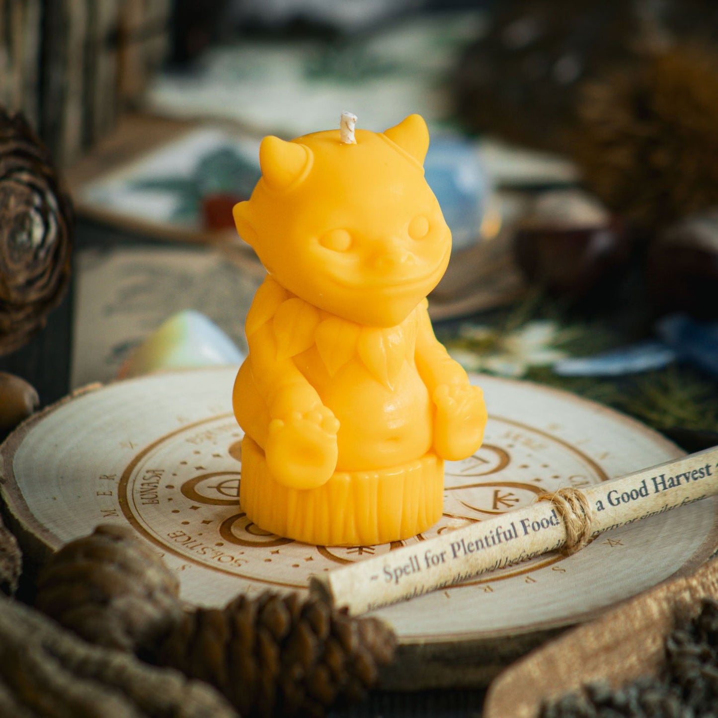 A bright yellow candle in the shape of a magical nature sprite sits behind a rolled up spell to celebrate Mabon