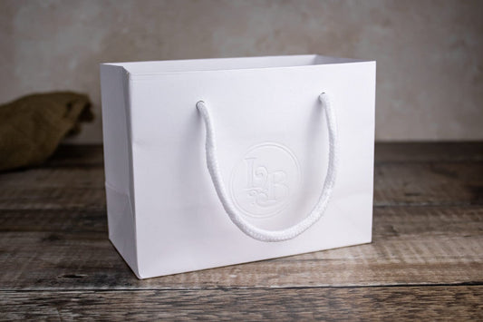 A white paper gift bag with corded handles sits on a wooden table