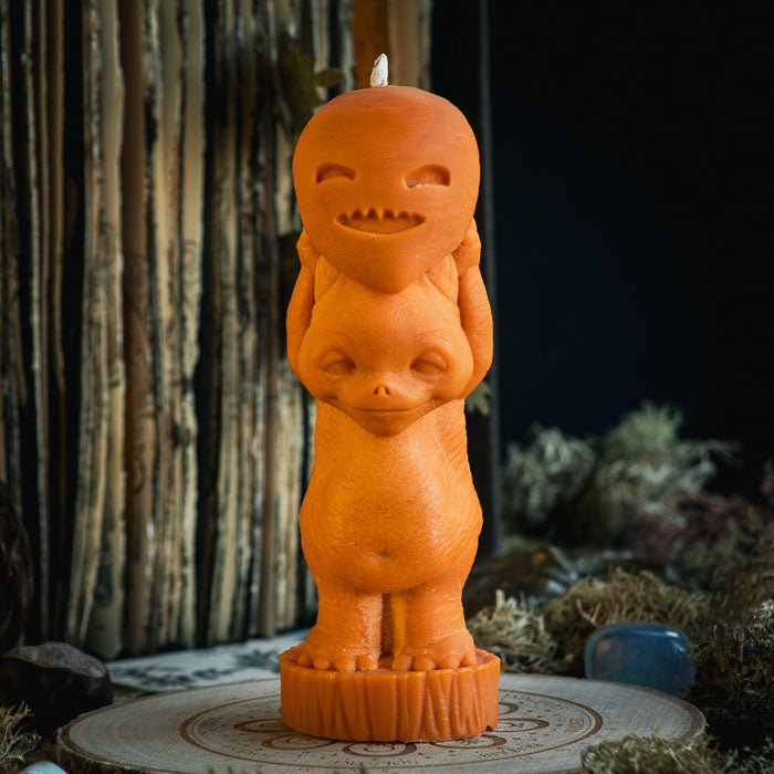 A vibrant orange pillar candle in the shape of a cute magical creature representing Halloween