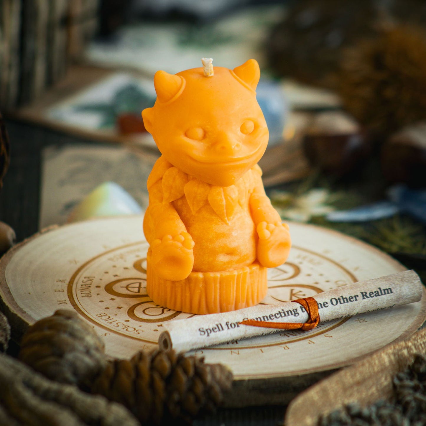 A vibrant orange candle in the shape of a magical nature sprite sits behind a rolled up spell to celebrate Halloween