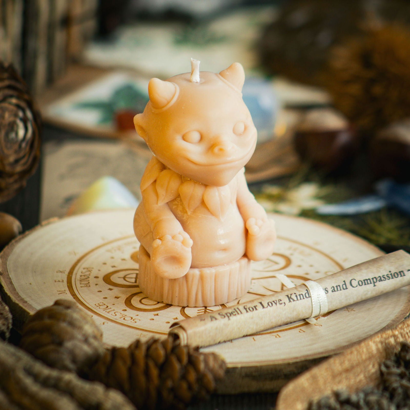 A striking pink summer candle in the shape of a magical nature sprite sits behind a rolled up spell to celebrate Lugnasadh