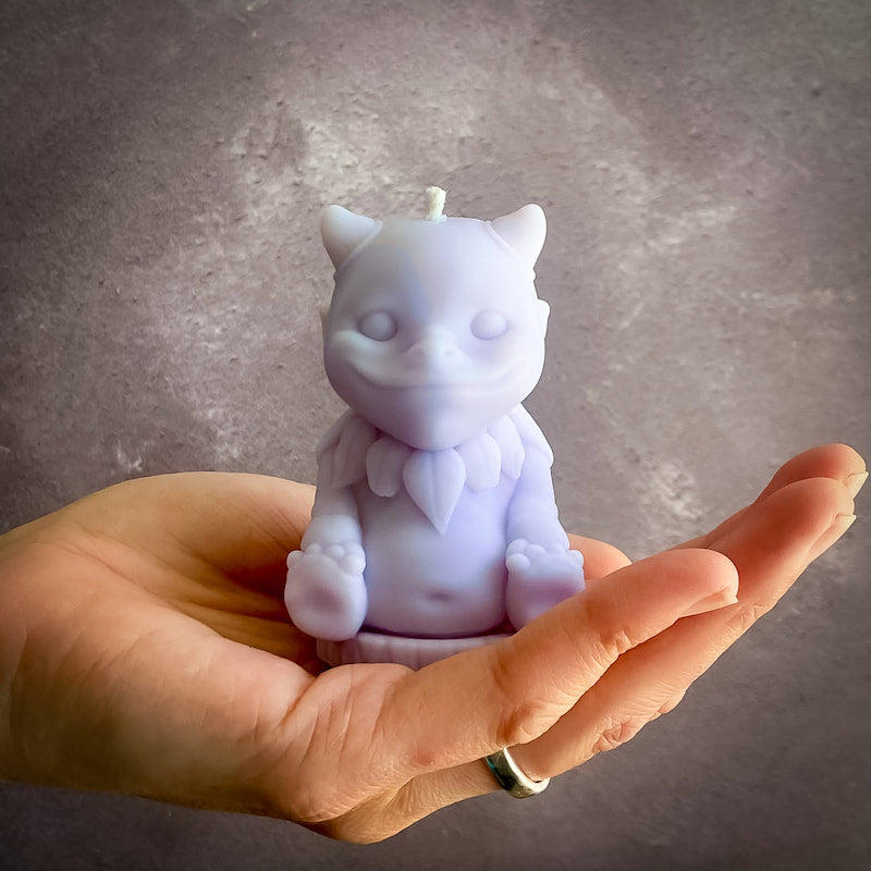 A pale lavender candle in the shape of a cute mythical creature sits in the palm of a hand