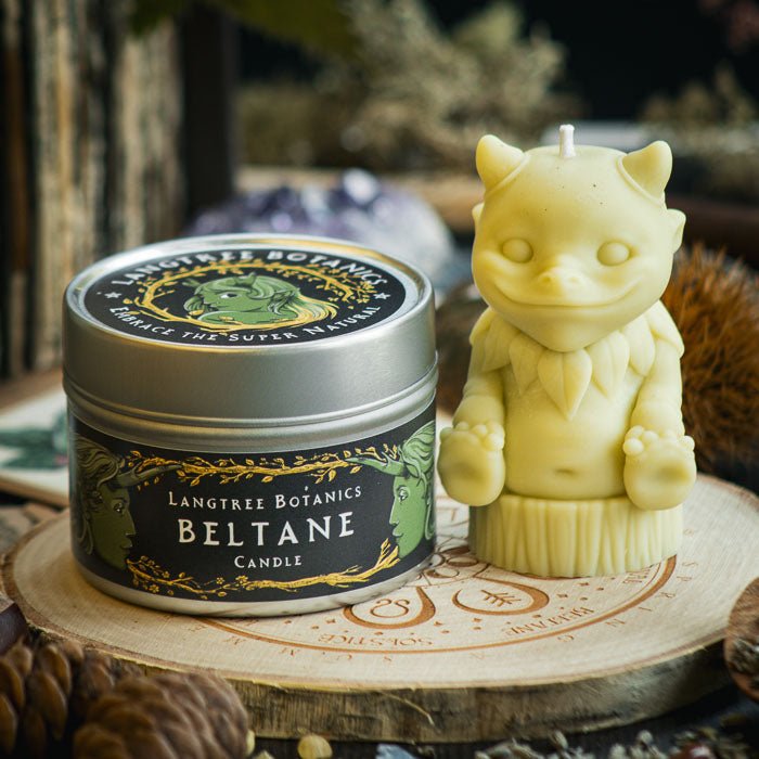 A metal tin container candle sat next to a green woodland creature candle on a wooden placemat