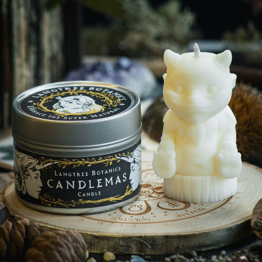 A metal tin container candle sat next to a white woodland creature candle on a wooden placemat