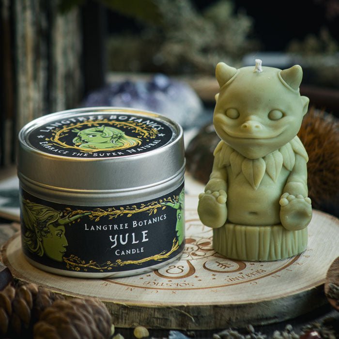 A metal tin container candle sat next to a green woodland creature candle on a wooden placemat