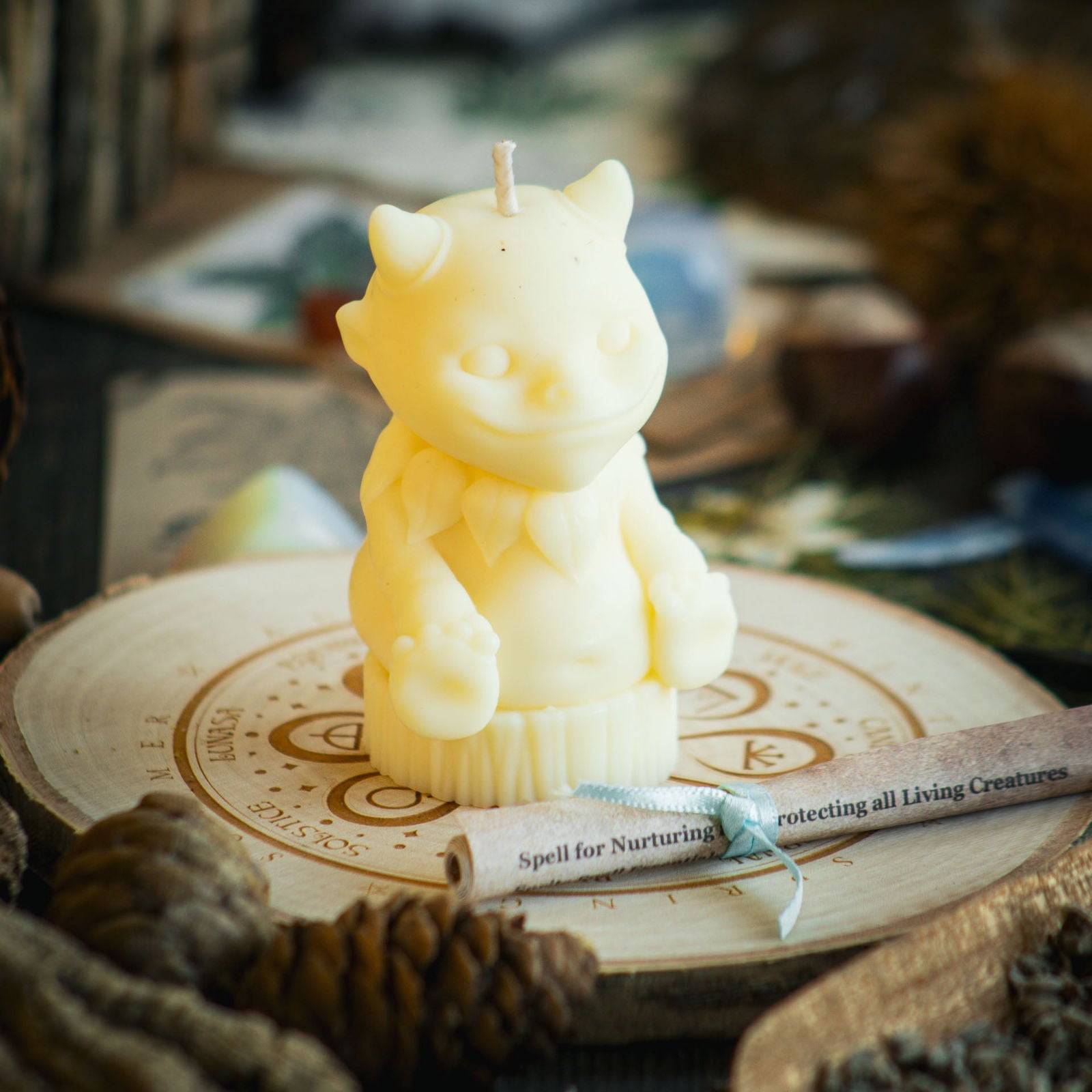 A pale yellow candle in the shape of a magical nature sprite sits behind a rolled up spell to celebrate spring equinox   