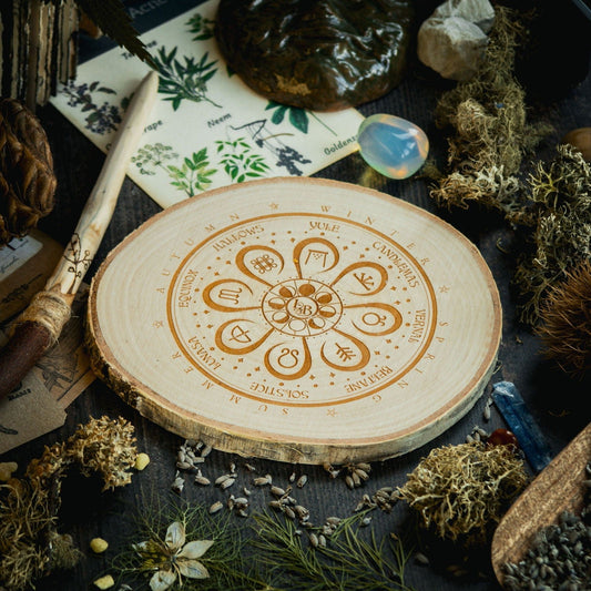 A decorative wooden log slice depicting the pagan wheel-of-the-year surrounded by seasonal foliage and healing crystals