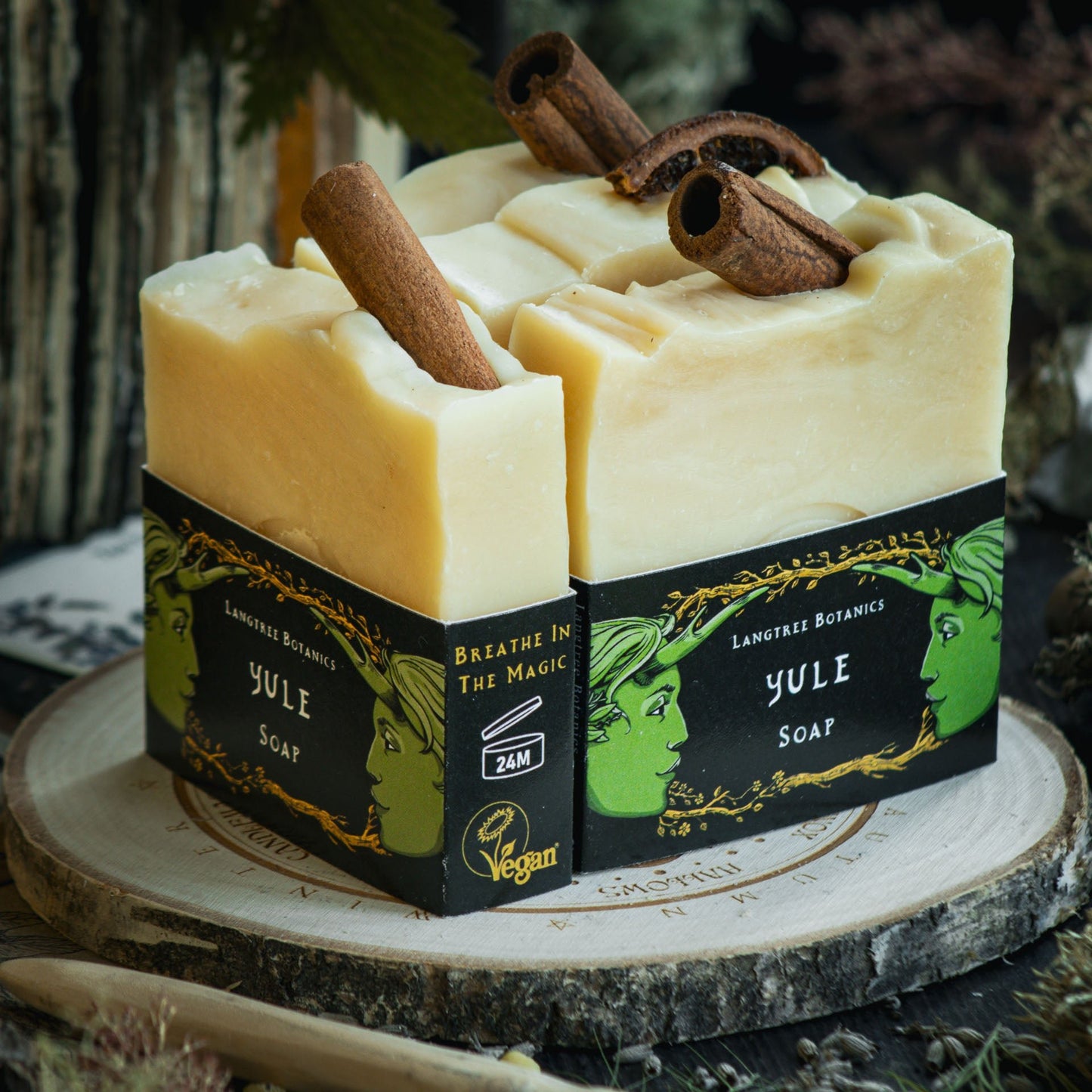 Four bars of Yule soap on top of a decorative wheel-of-the-year log slice surrounded by seasonal foliage.